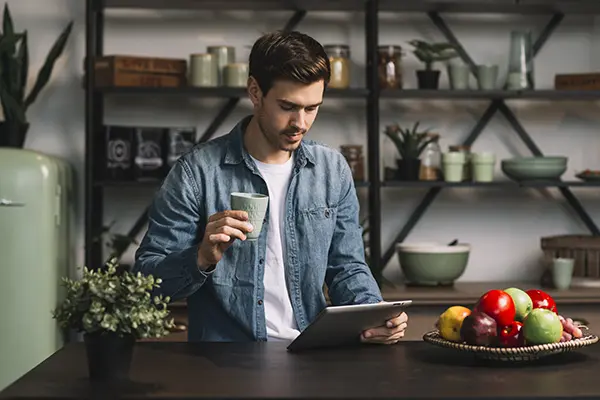 Man holding cup coffee looking at a digital tablet